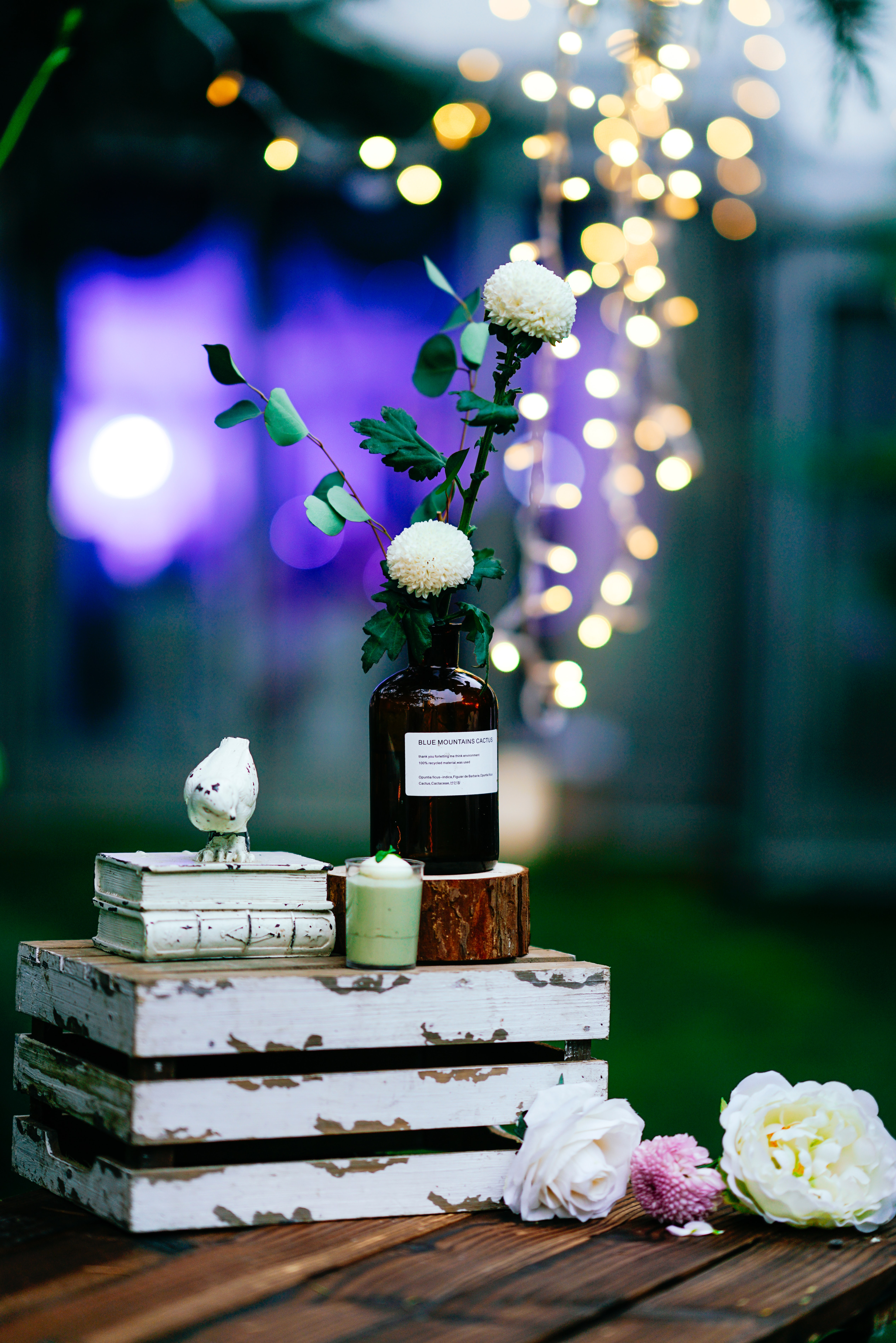 2 small books next to brown glass bottle with white florals on wood piece on upside down crate