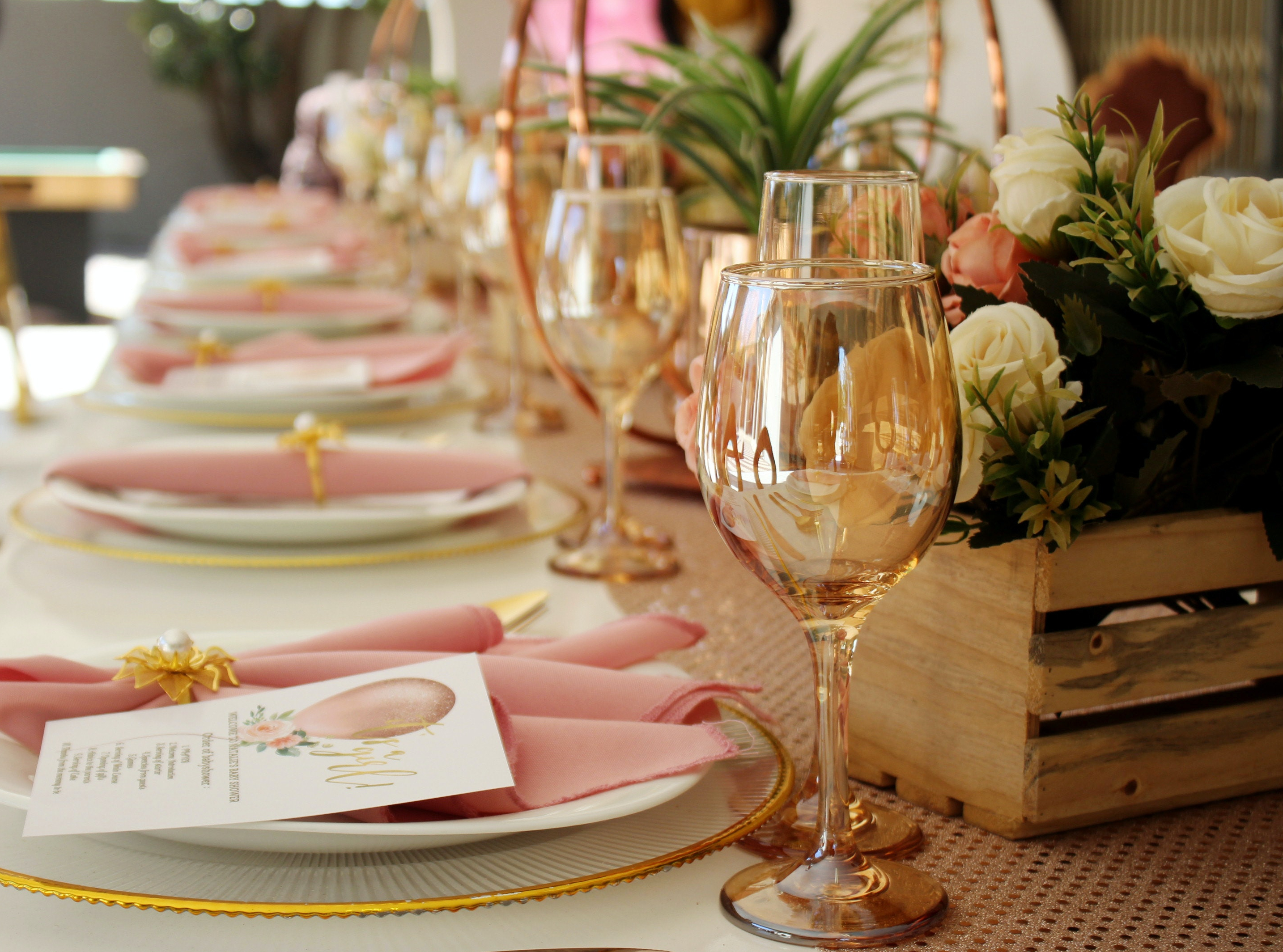 Table Setting with amber gold glasses, rose coloured napkins and wooden crates filled with flowers