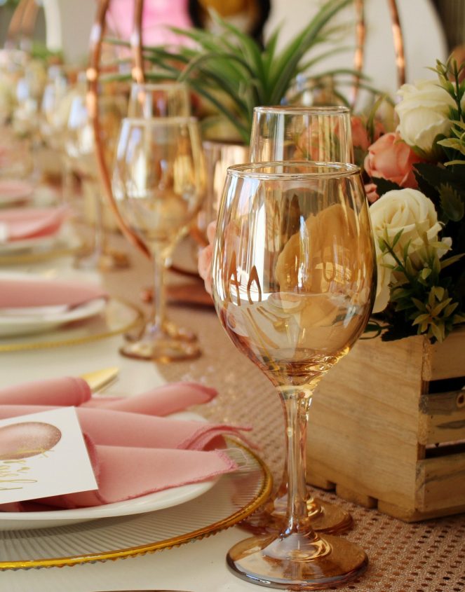 Table Setting with amber gold glasses, rose coloured napkins and wooden crates filled with flowers