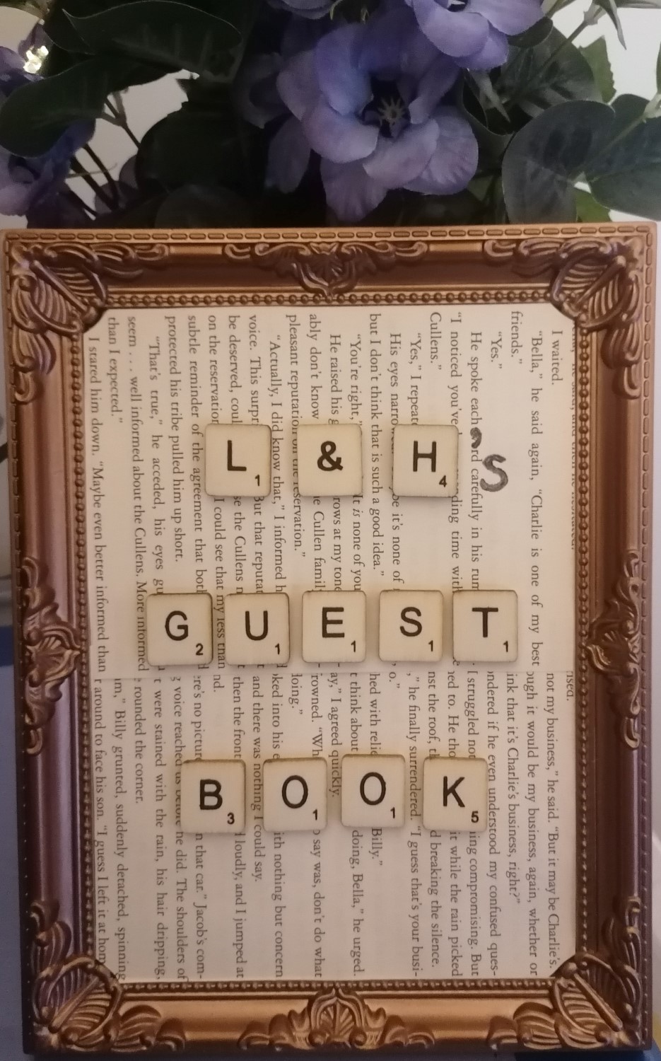 Gold picture frame with scrabble letters on book pages spelling out L&H's Guest Book